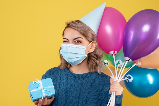 junge Frau, die Luftballons und wenig Geschenk auf Gelb hält