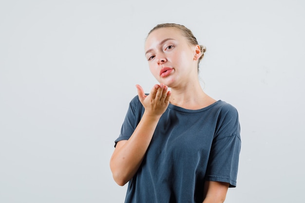 Junge Frau, die Luftkuss im grauen T-Shirt sendet und charmant aussieht