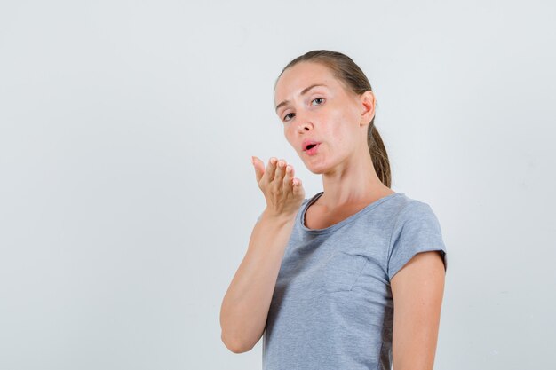 Junge Frau, die Luftkuss in der grauen T-Shirt-Vorderansicht sendet.