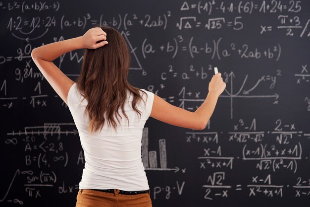 Junge Frau, die Matheproblem auf Tafel betrachtet