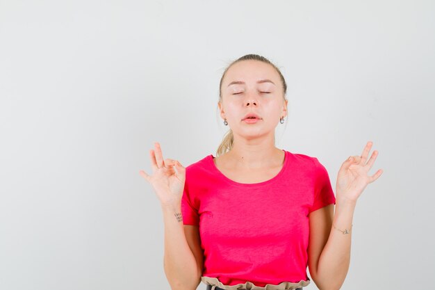 Kostenloses Foto junge frau, die meditation mit geschlossenen augen im t-shirt tut und ruhig schaut