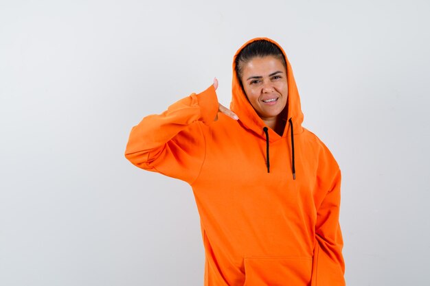 Kostenloses Foto junge frau, die mich anruft, geste in orangefarbenem hoodie und schön aussehend