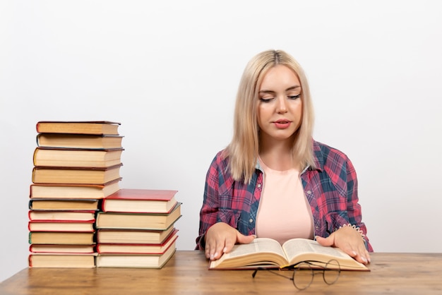 junge Frau, die mit Büchern sitzt und auf Weiß liest