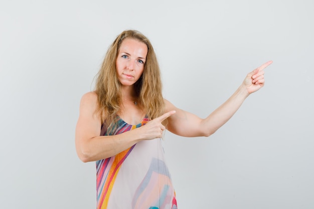 Kostenloses Foto junge frau, die mit den fingern im sommerkleid zur seite zeigt und selbstbewusst aussieht.