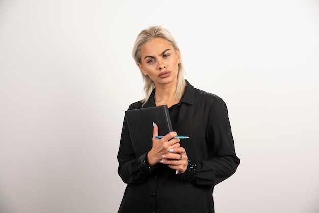 Junge Frau, die mit einem Bleistift und Zwischenablage auf weißem Hintergrund aufwirft. Hochwertiges Foto