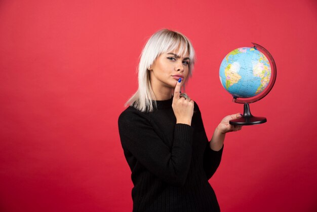 Junge Frau, die mit einem Globus auf einem roten Hintergrund aufwirft. Hochwertiges Foto