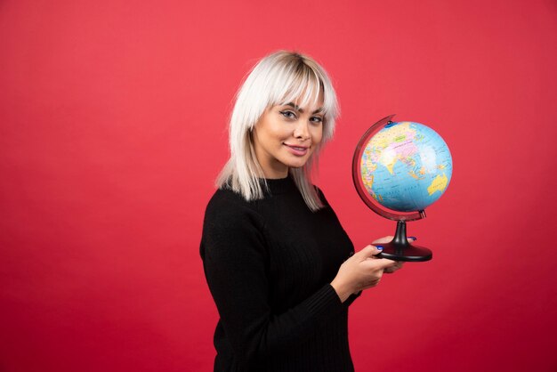 Junge Frau, die mit einem Globus auf einem roten Hintergrund aufwirft. Hochwertiges Foto