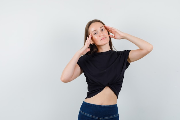 Junge Frau, die mit Händchenhalten auf ihrem Kopf in der schwarzen Bluse aufwirft und gut aussieht.