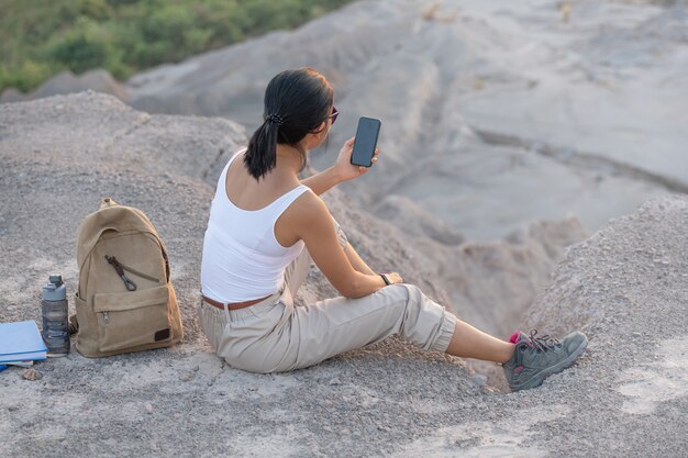 Junge Frau, die mit Handy sitzt. Hoher Gebirgstouristenweg bei Sonnenuntergang.