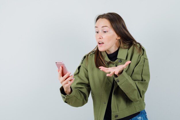 Junge Frau, die mit jemandem während des Videoanrufs in der grünen Jacke, Vorderansicht argumentiert.