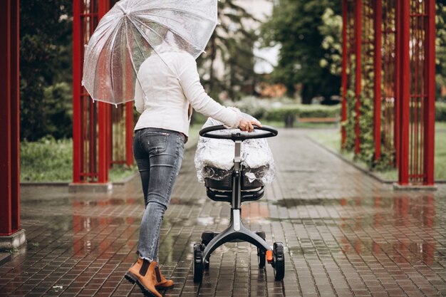 Junge Frau, die mit Kinderwagen unter dem Regenschirm in einem regnerischen Wetter geht