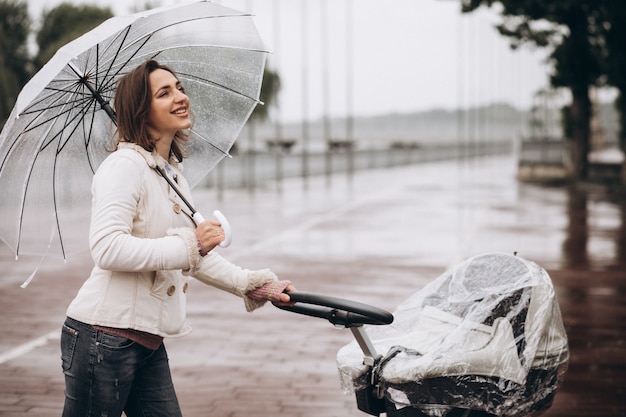 Junge Frau, die mit Kinderwagen unter dem Regenschirm in einem regnerischen Wetter geht