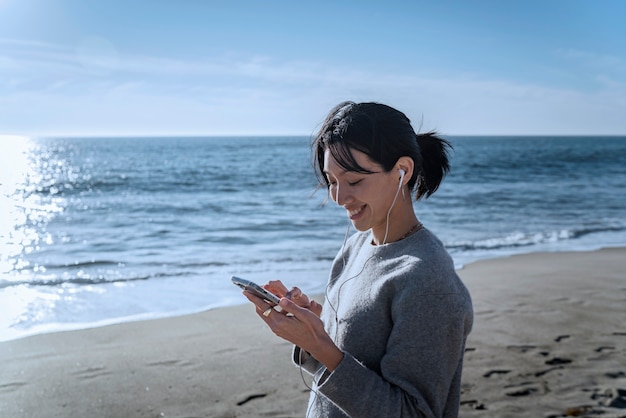 Junge Frau, die mit Kopfhörern Musik auf dem Smartphone am Strand hört