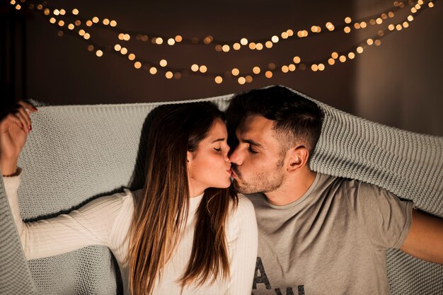 Junge Frau, die mit Mann in der Bettdecke küsst