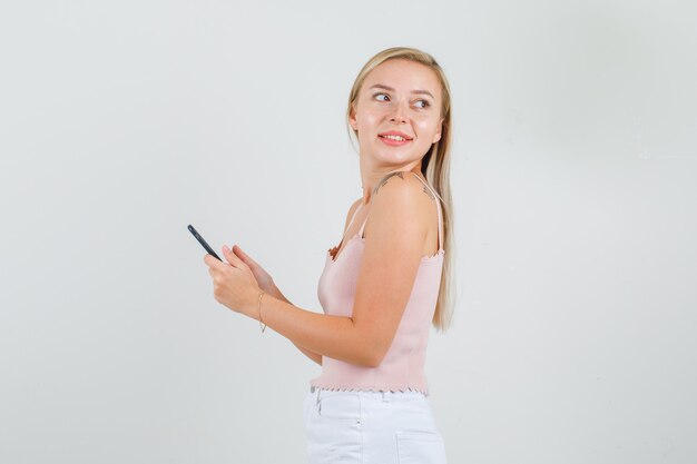 Junge Frau, die mit Smartphone in der Hand im Unterhemd zurückblickt