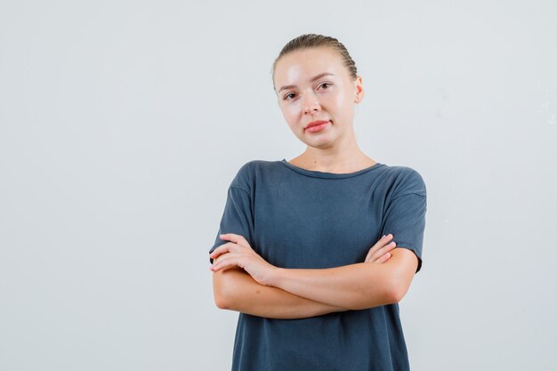 Junge Frau, die mit verschränkten Armen im grauen T-Shirt steht und zuversichtlich schaut