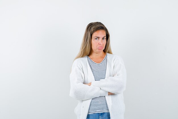 Junge Frau, die mit verschränkten Armen im T-Shirt, in der Jacke steht und unzufrieden schaut, Vorderansicht.