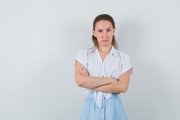 Junge Frau, die mit verschränkten Armen in Bluse, Rock und nachdenklich aussehend steht