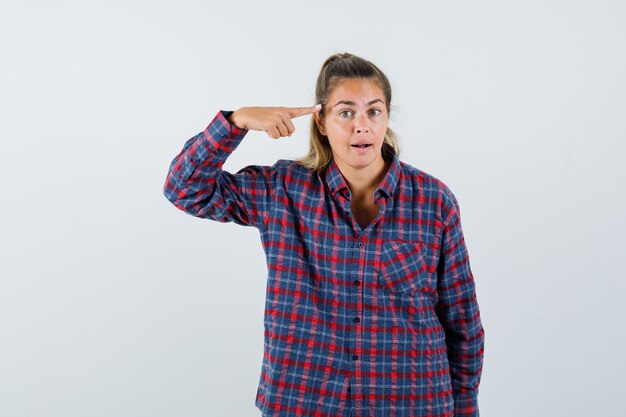 Junge Frau, die mit Zeigefinger im karierten Hemd auf sich selbst zeigt und ernst aussieht