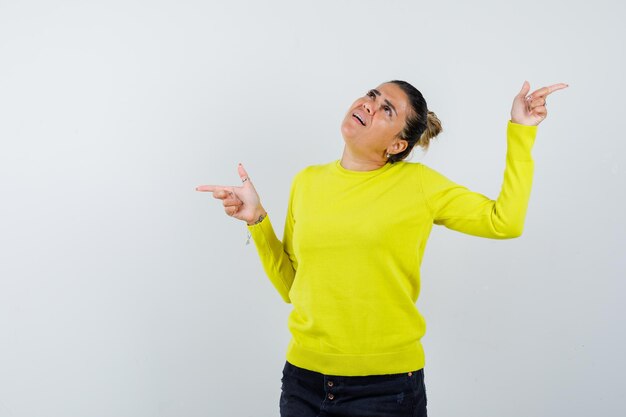 Junge Frau, die mit Zeigefingern in gelbem Pullover und schwarzer Hose nach links und rechts zeigt und gehetzt aussieht