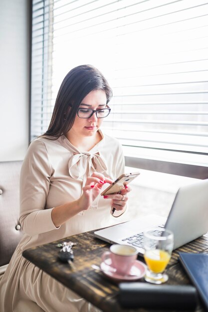 Junge Frau, die Mobiltelefon in der Kaffeestube verwendet