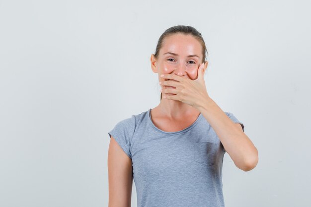 Junge Frau, die Mund beim Lachen im grauen T-Shirt, Vorderansicht bedeckt.