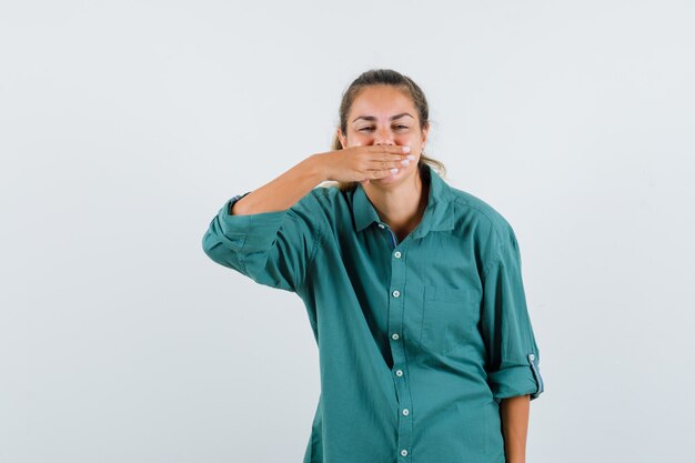 Junge Frau, die Mund mit Hand in grüner Bluse bedeckt und niedlich schaut