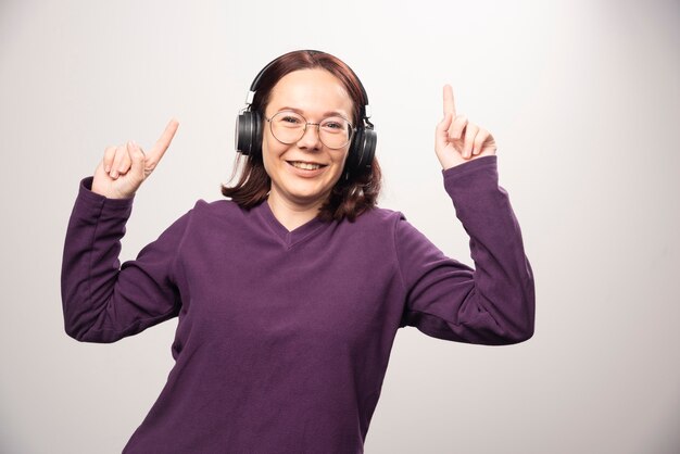 Junge Frau, die Musik in den Kopfhörern auf einem weißen Hintergrund tanzt und hört. Hochwertiges Foto