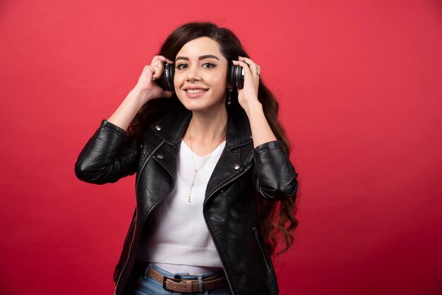 Junge Frau, die Musik über Kopfhörer hört und auf einem roten Hintergrund aufwirft. Foto in hoher Qualität