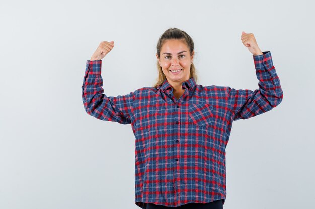 Junge Frau, die Muskeln im karierten Hemd zeigt und mächtig aussieht