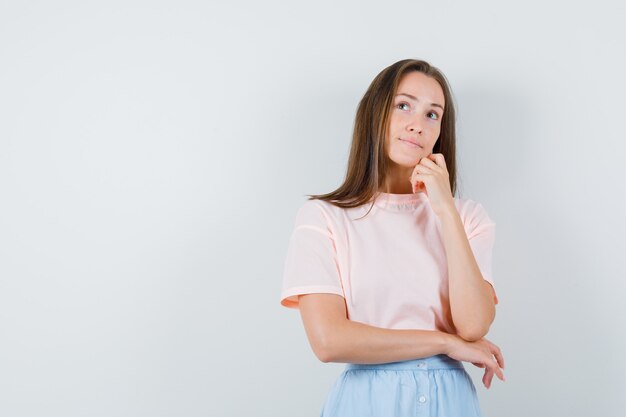 Junge Frau, die nach oben in T-Shirt, Rock und nachdenklich, Vorderansicht schaut.