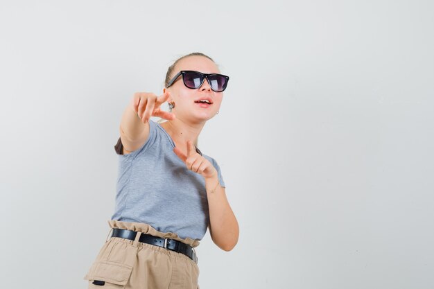 Junge Frau, die nach vorne in T-Shirt, Hosen zeigt und fröhlich schaut, Vorderansicht.