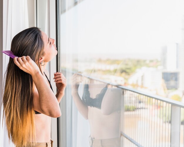 Junge Frau, die nahe dem Balkon kämmt ihr Haar steht