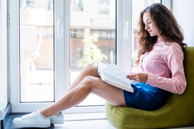 Junge Frau, die nahe Fenster studiert