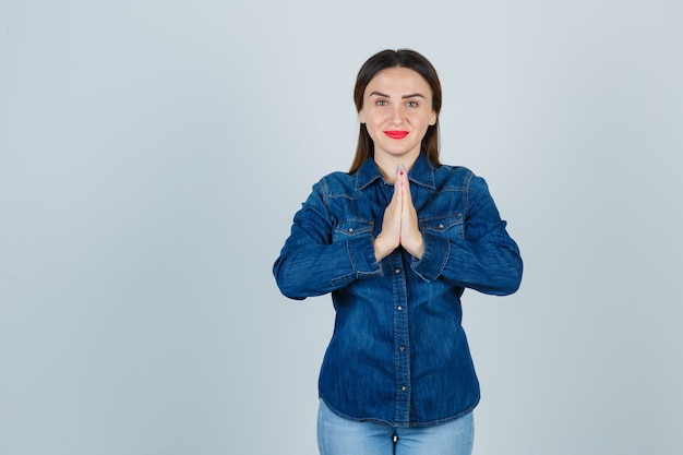 Junge Frau, die namaste Geste in Jeanshemd und in Jeans zeigt und friedlich schaut