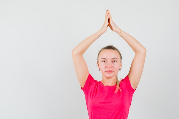 Junge Frau, die namaste Geste über ihrem Kopf in der Vorderansicht des T-Shirts und der Hose zeigt