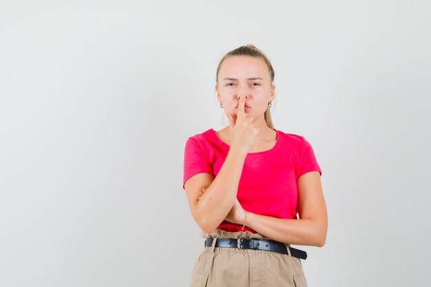 Junge Frau, die Nase mit Finger im T-Shirt und in der Hose berührt