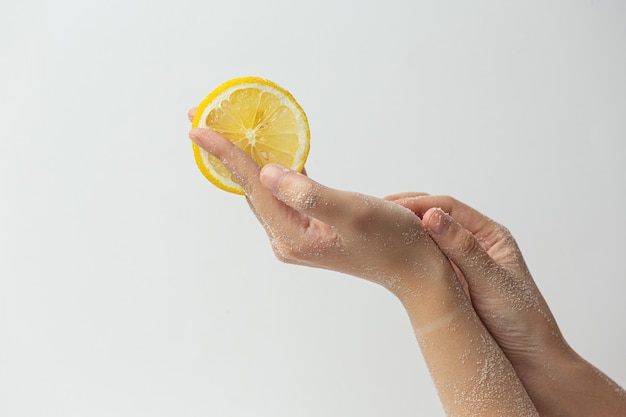 Junge Frau, die natürliches Zitronenpeeling auf Händen gegen weiße Oberfläche anwendet