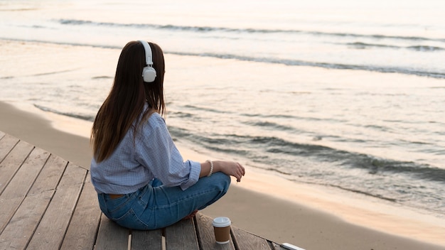 Junge Frau, die neben Meer meditiert, während sie Kopfhörer trägt