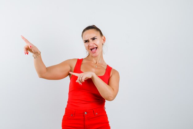 Junge Frau, die oben im roten Trägershirt, in den Hosen und in der lustigen Vorderansicht zeigt.