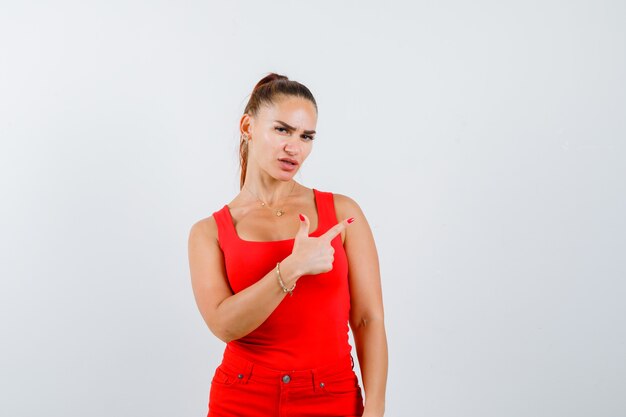 Junge Frau, die oben im roten Trägershirt, in der Hose und in der nachdenklichen Vorderansicht zeigt.