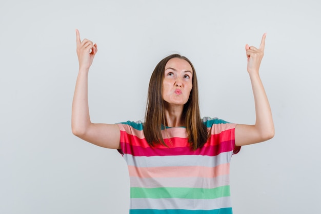 Junge Frau, die oben im T-Shirt zeigt und unzufrieden aussieht, Vorderansicht.