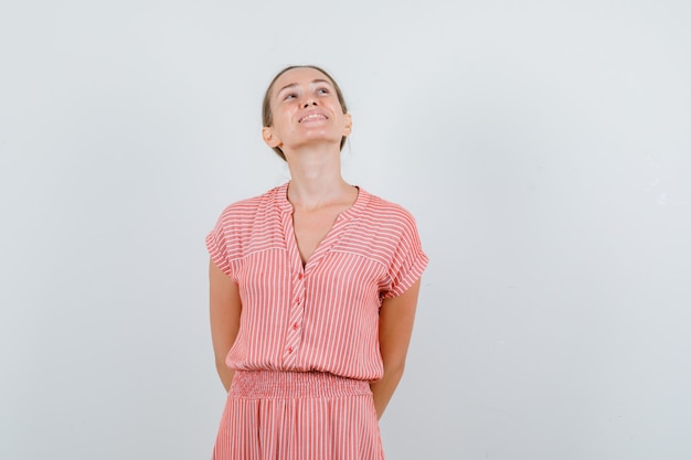 Junge Frau, die oben mit den Händen auf im gestreiften Kleid schaut und glückliche Vorderansicht schaut.