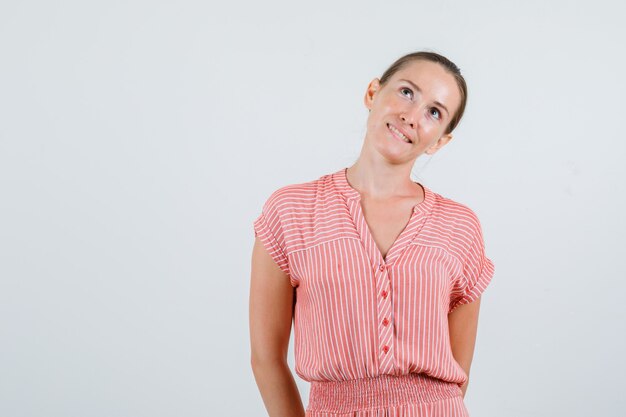 Junge Frau, die oben mit den Händen auf im gestreiften Kleid schaut und verträumte Vorderansicht schaut.