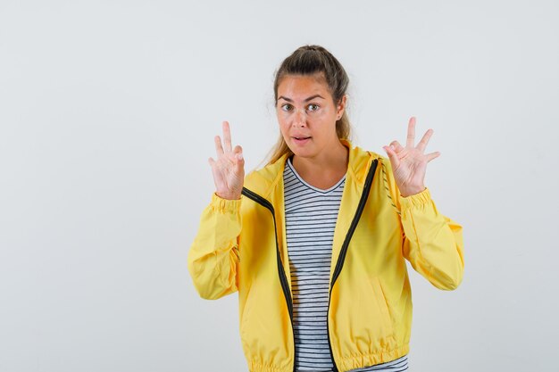 Junge Frau, die ok Geste in T-Shirt, Jacke zeigt und selbstbewusst aussieht. Vorderansicht.