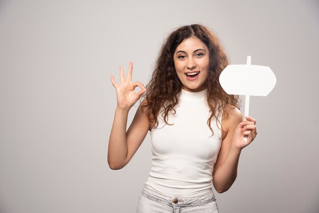 Junge Frau, die ok Geste zeigt und ein leeres weißes Plakat hält. Hochwertiges Foto