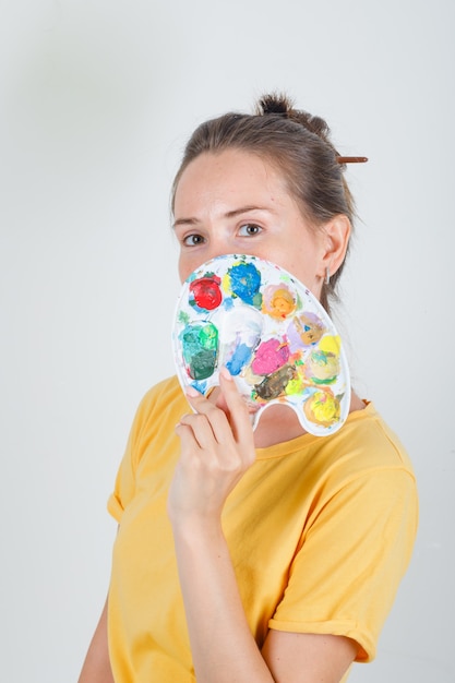 Junge Frau, die Palette über Gesicht im gelben T-Shirt hält