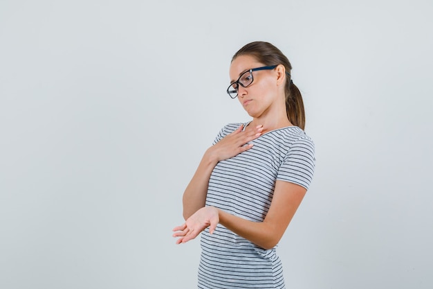 Junge Frau, die Palme im gestreiften T-Shirt, in der Brille zeigt und nachdenklich schaut. Vorderansicht.