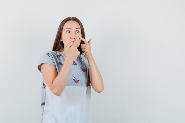 Junge Frau, die Pickel von ihrem Gesicht in der T-Shirt-Vorderansicht entfernt.