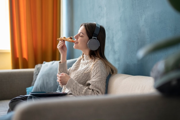 Junge Frau, die Pizza isst und Musik hört